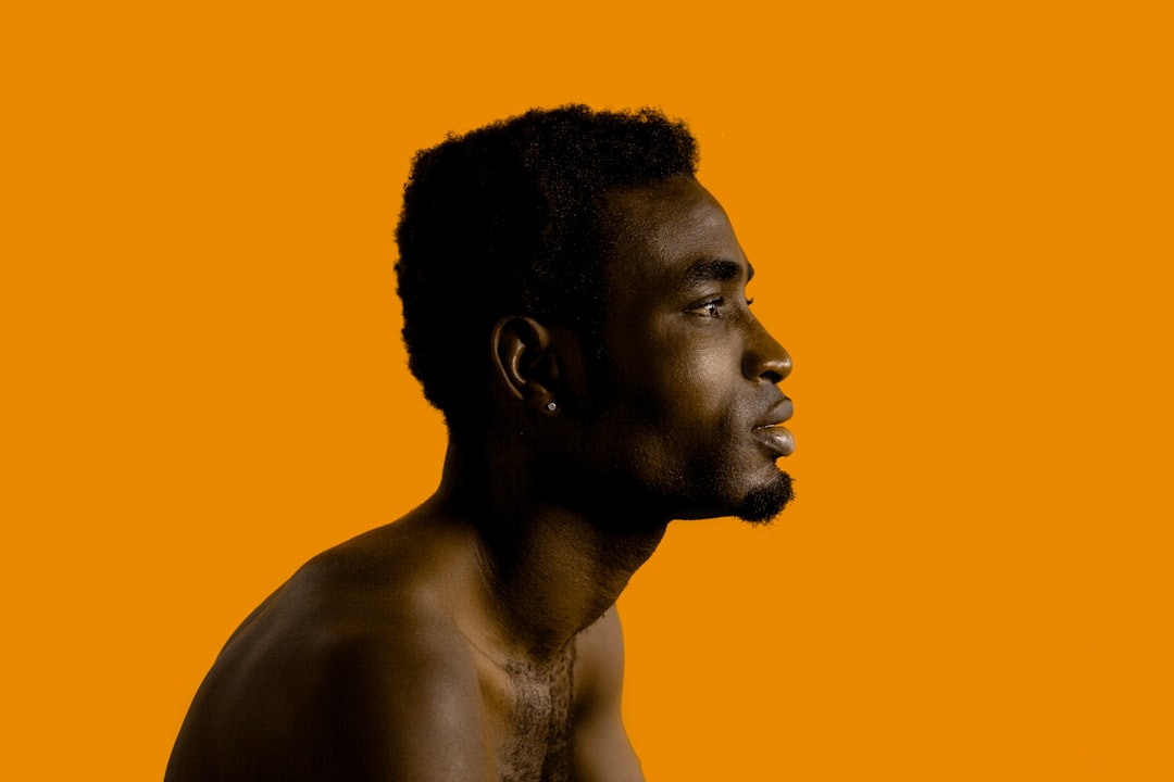 A man with no shirt standing in front of an orange background